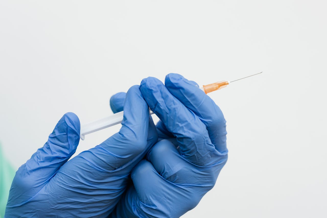 Close-up of Holding a Syringe While Wearing Blue Gloves